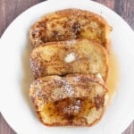 French Toast with butter, maple syrup and confectioners sugar on a white plate.
