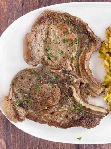 Pan seared pork chops on a white plate.