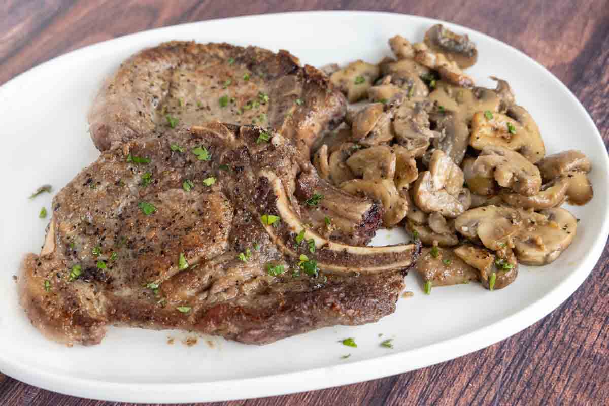 Pan seared pork chops with sautéed mushrooms on a white plate.