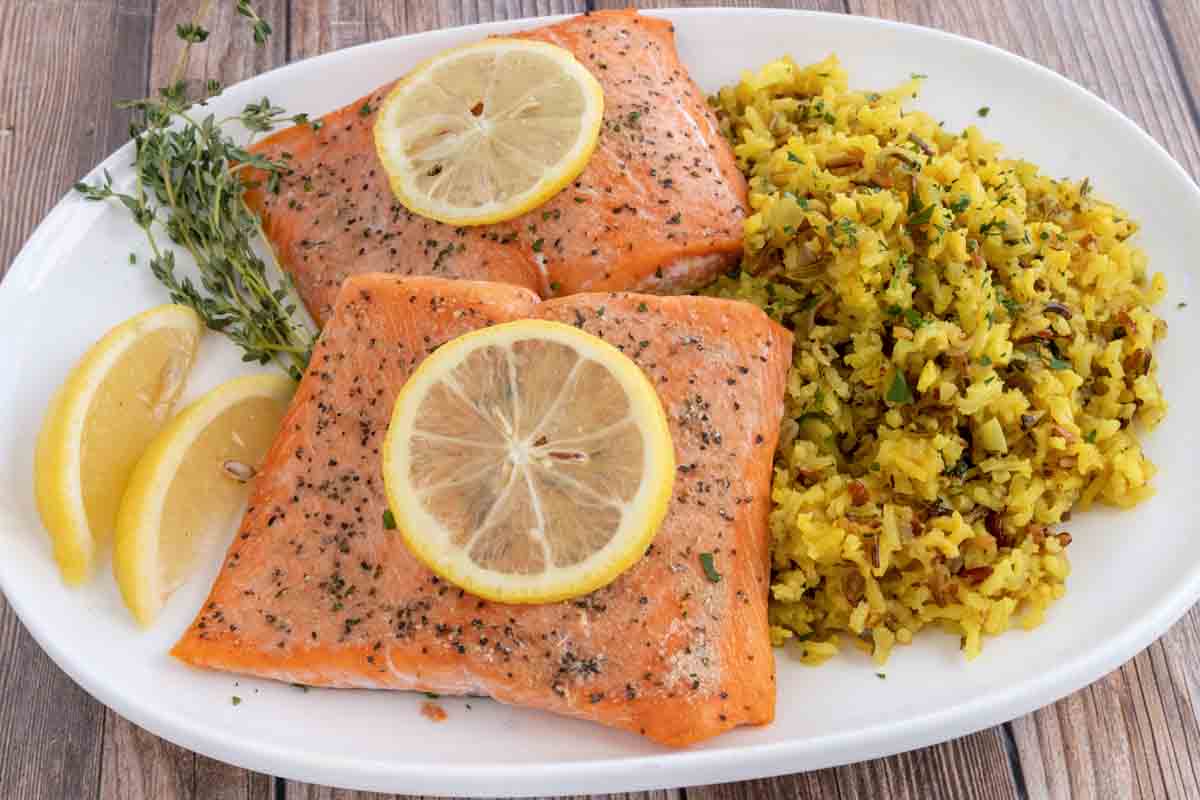 baked salmon with lemon on top and rice on a white plate