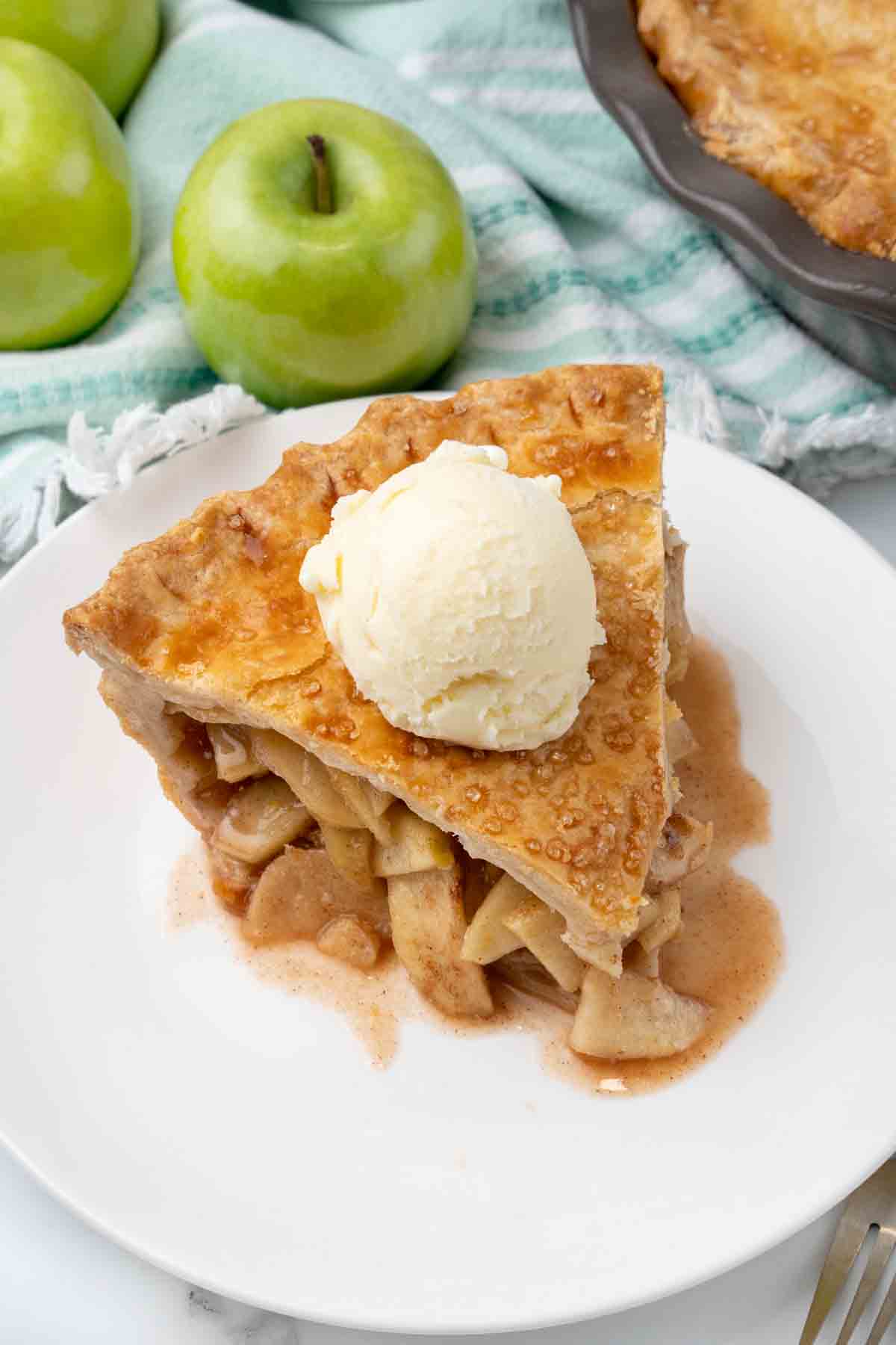 Slice of apple pie with vanilla ice cream on a white plate.