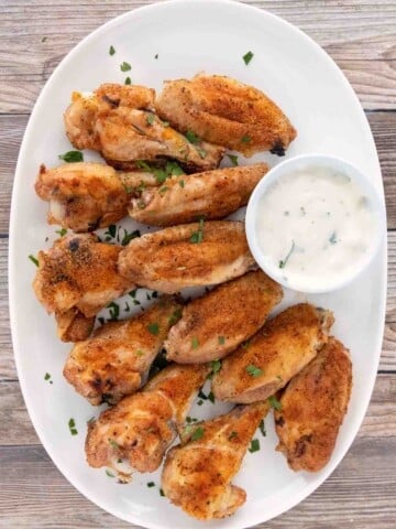Crispy baked chicken wings with ranch dressing on a white platter.