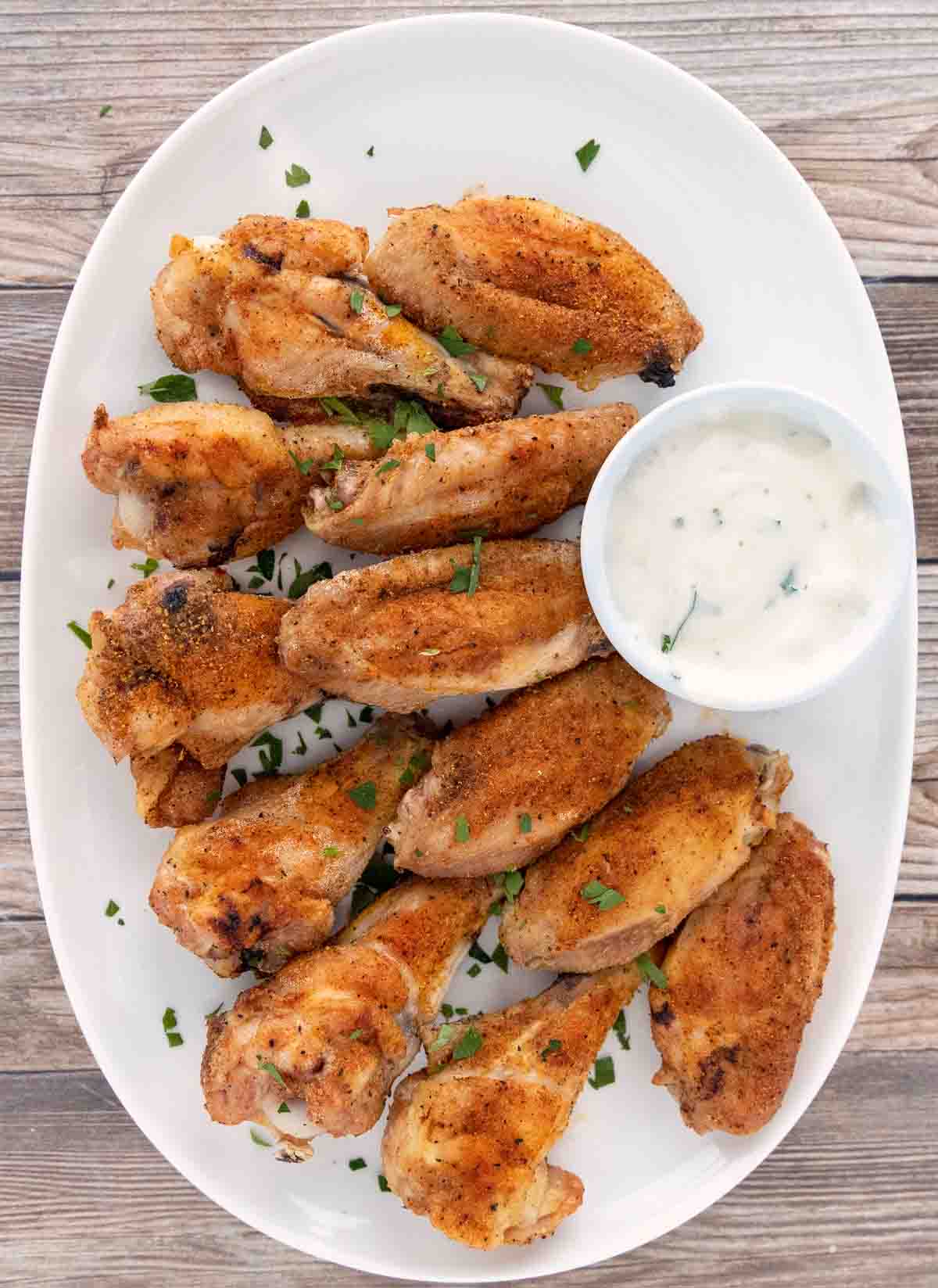 Crispy baked chicken wings with ranch dressing on a white platter.