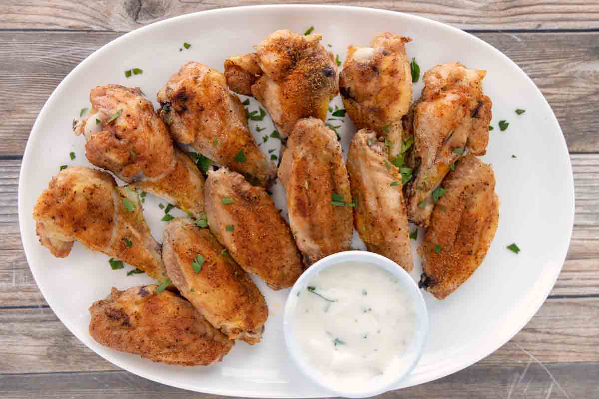 Crispy baked chicken wings with ranch dressing on a white platter.