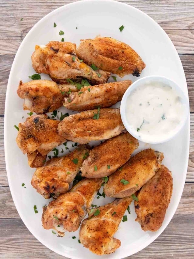 Crispy baked chicken wings with ranch dressing on a white platter.