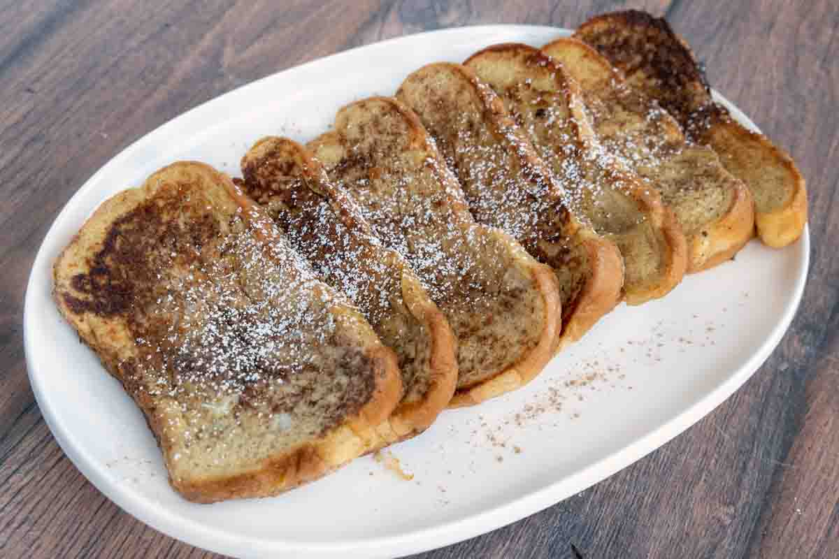 French toast with confectioners sugar on a white platter.