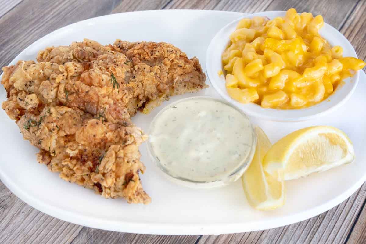 Crispy fried catfish on a white plate with mac and cheese and tarter sauce.