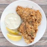 Crispy fried catfish on a white plate with lemon wedges and tarter sauce