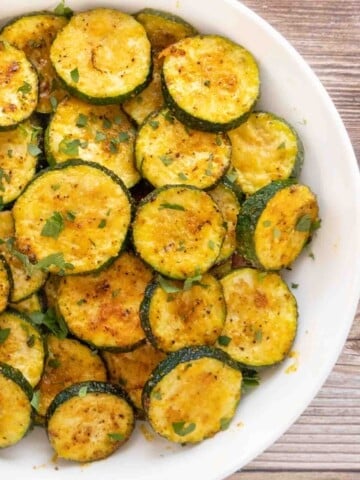 Oven roasted zucchini in a white bowl.