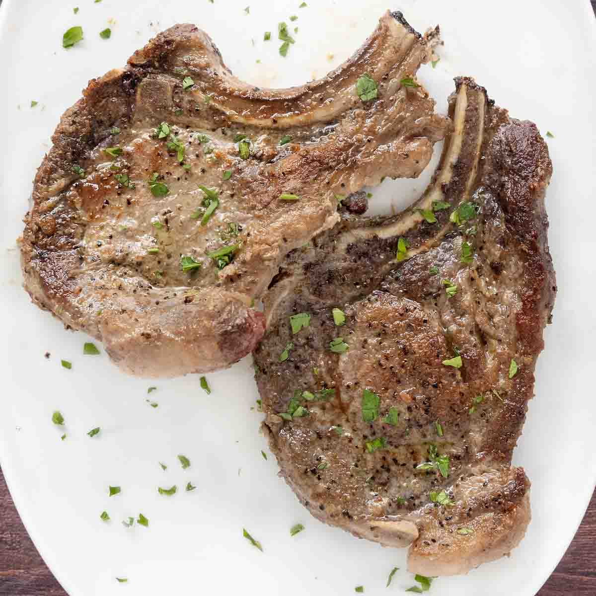 Pan seared pork chops on a white plate.