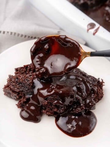 Chocolate pudding cake on a white plate with a spoon adding more of the syrup.
