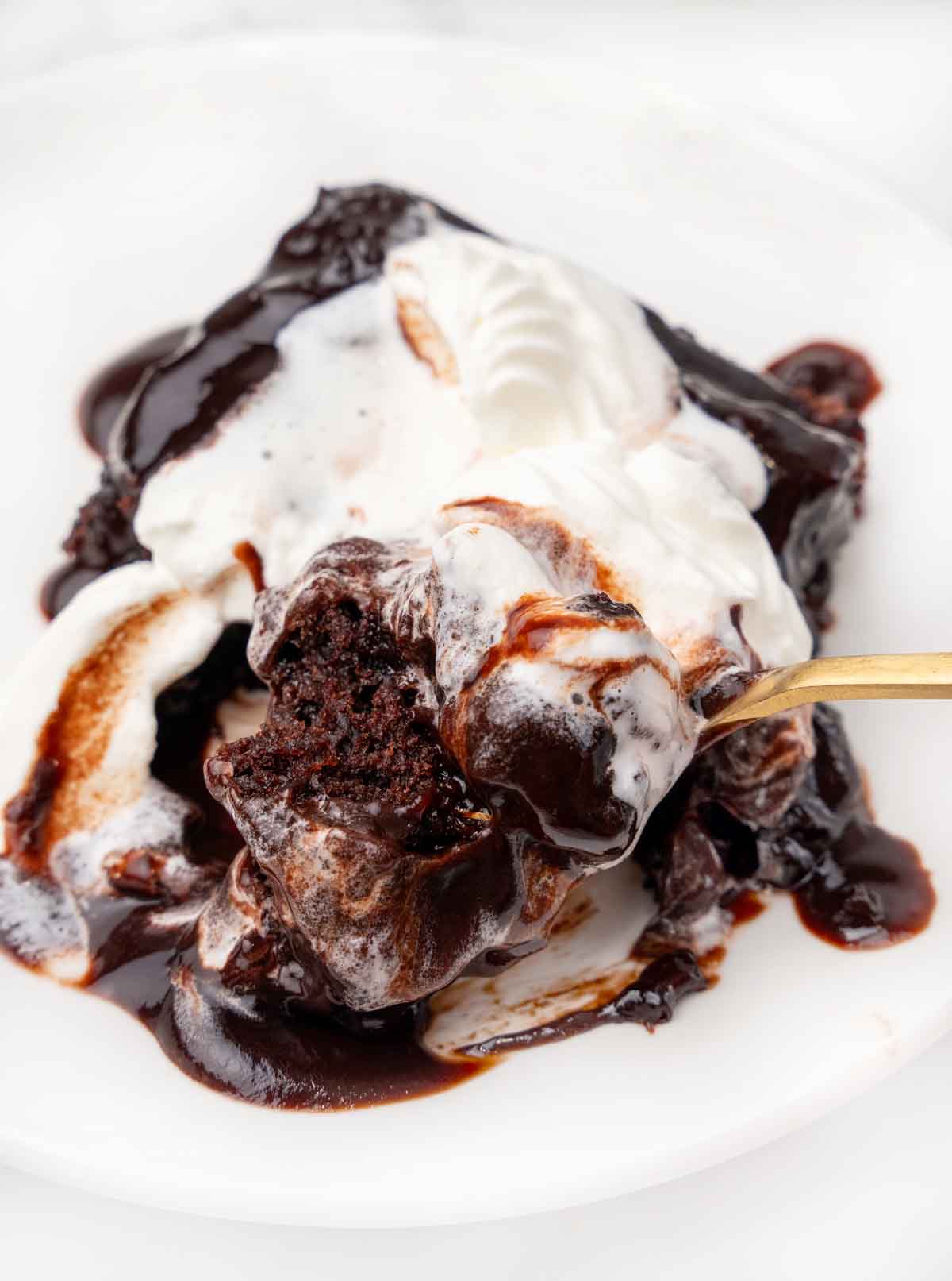 Chocolate pudding cake on a white plate with whipped cream and a spoon.