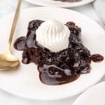 Chocolate pudding cake on a white plate with whipped cream.