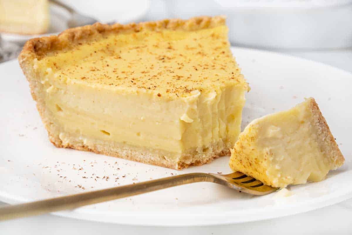 Slice of egg custard pie on a white plate with a fork taking a piece out of the slice.
