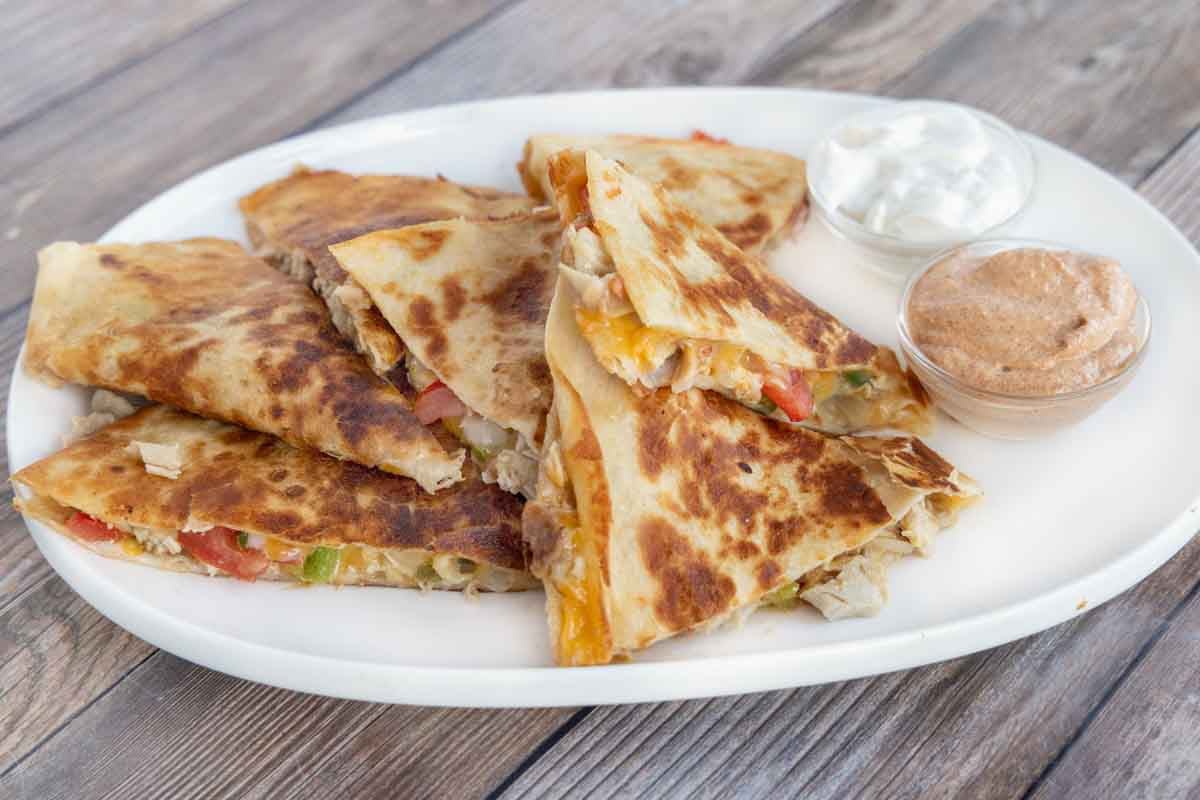 Chicken quesadilla cut into sections on a white platter with dipping sauces.