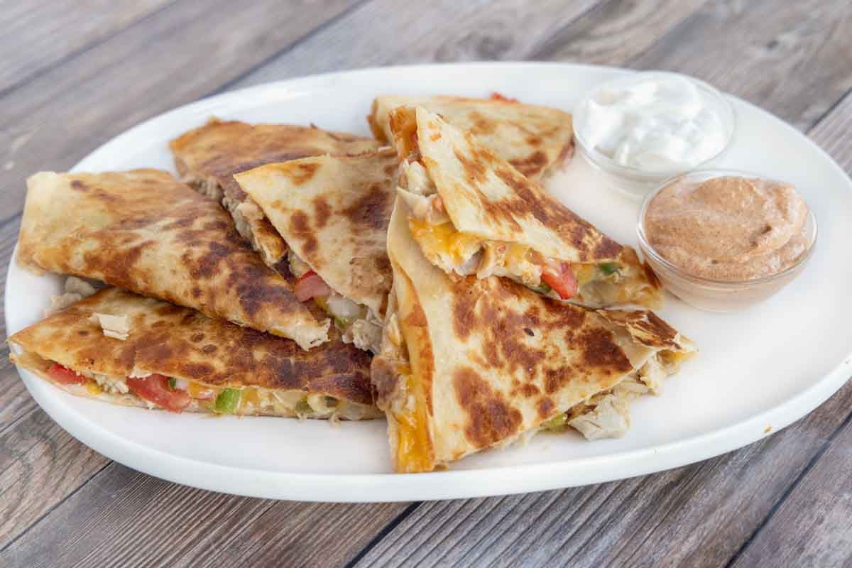 Quesadilla cut into sections on a white platter with dipping sauces.