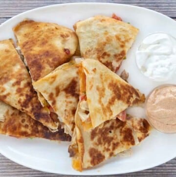 Chicken quesadilla cut into sections on a white platter with dipping sauces.