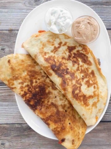 Two chicken quesadillas on a white platter with dipping sauces.