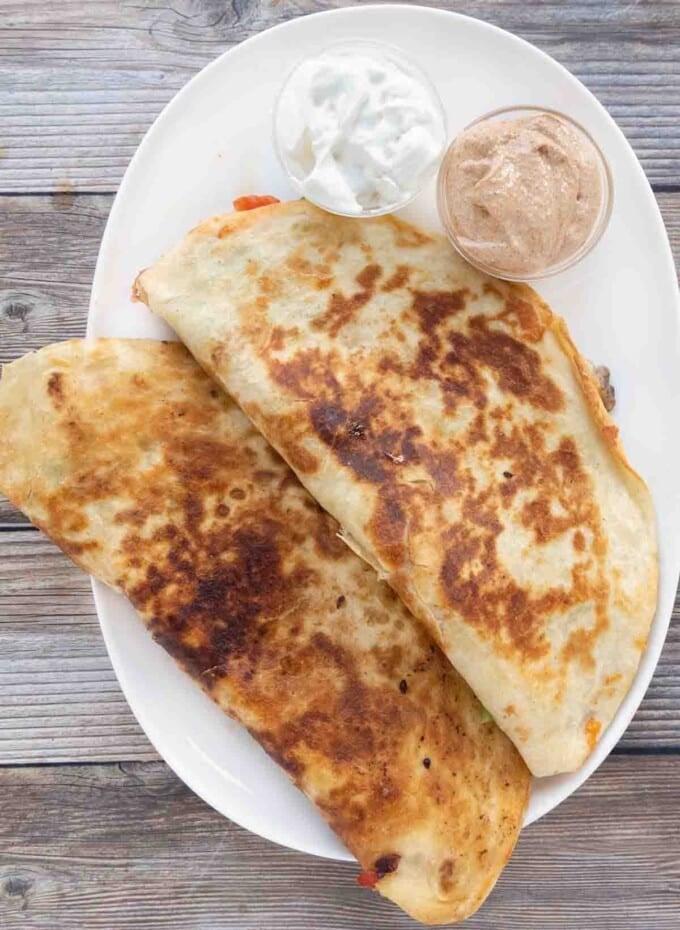 Two chicken quesadillas on a white platter with dipping sauces.