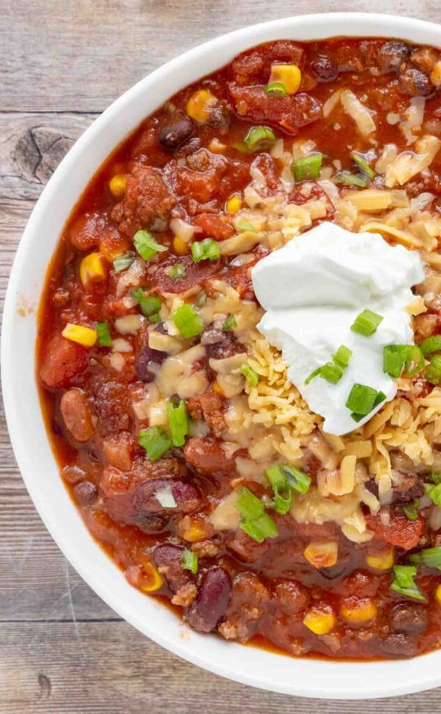 Slow cooker chili with shredded cheese and sour cream in a white bowl