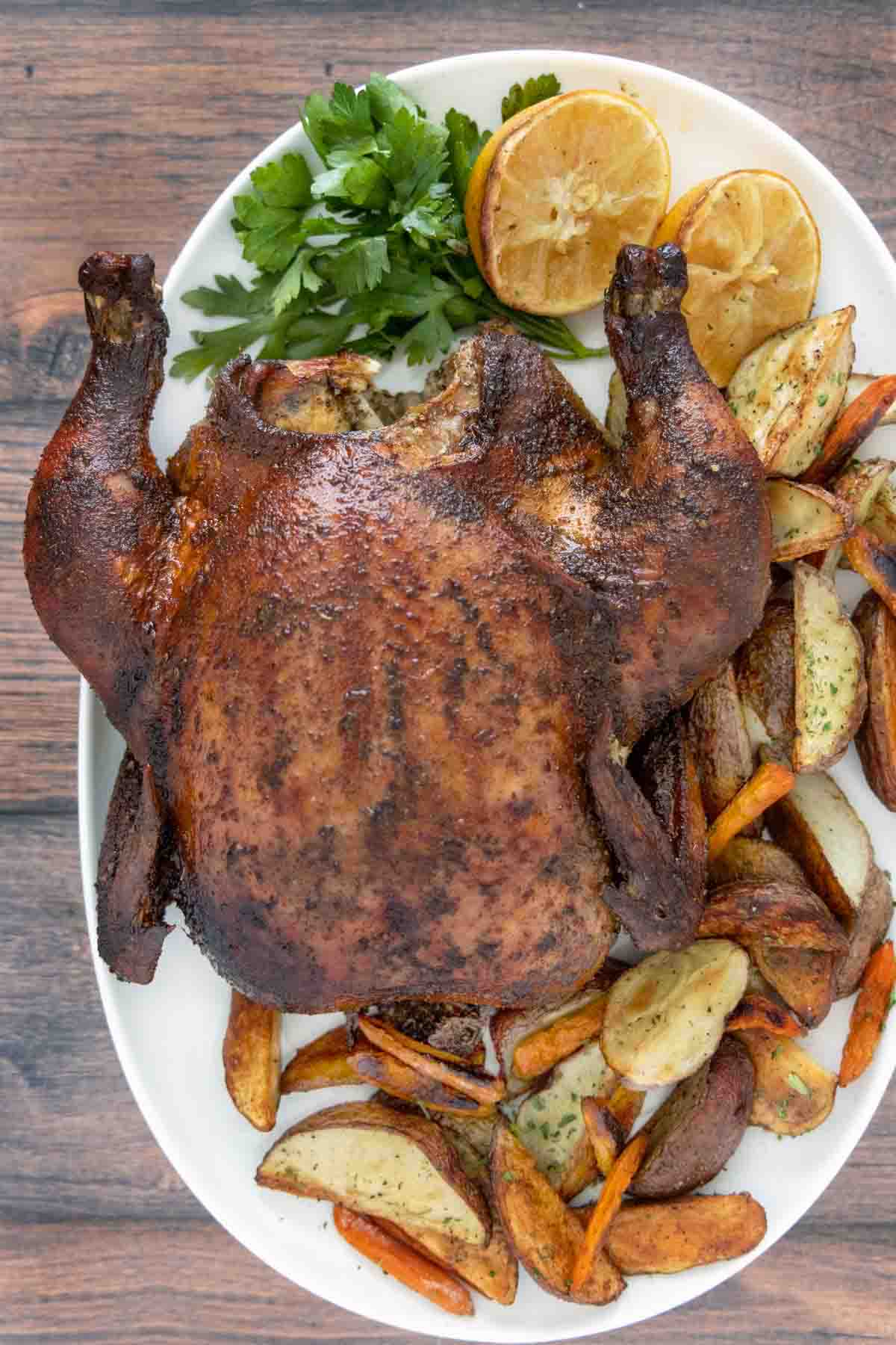Whole smoked chicken on white platter with roasted potatoes.