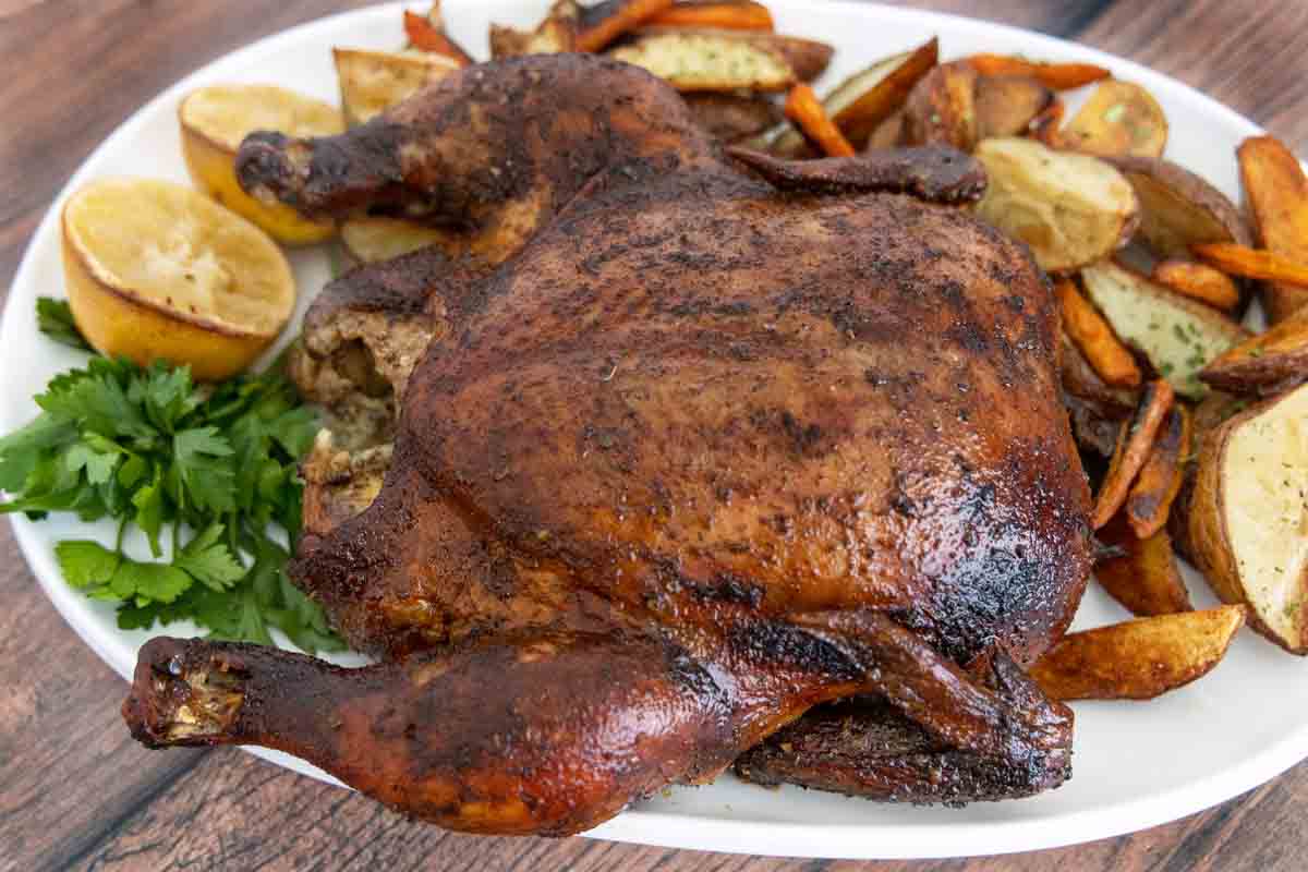 Whole smoked chicken on white platter with roasted potatoes.