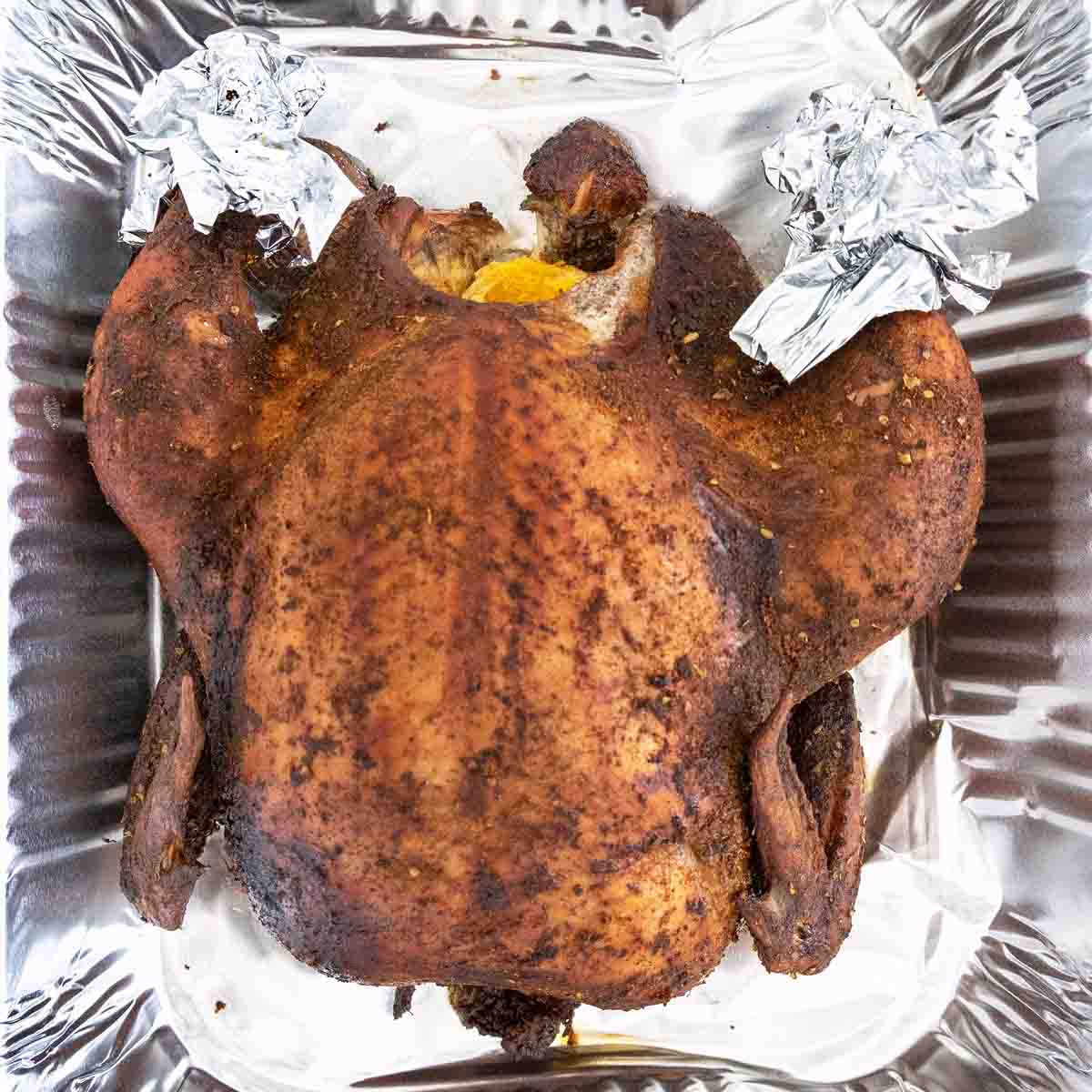 whole smoked chicken with legs ends wrapped in aluminum foil in a foil pan