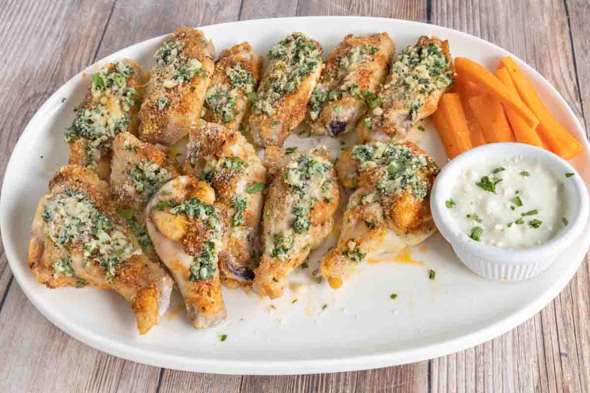 Garlic parmesan wings with carrot sticks and ranch dressing on a white platter.
