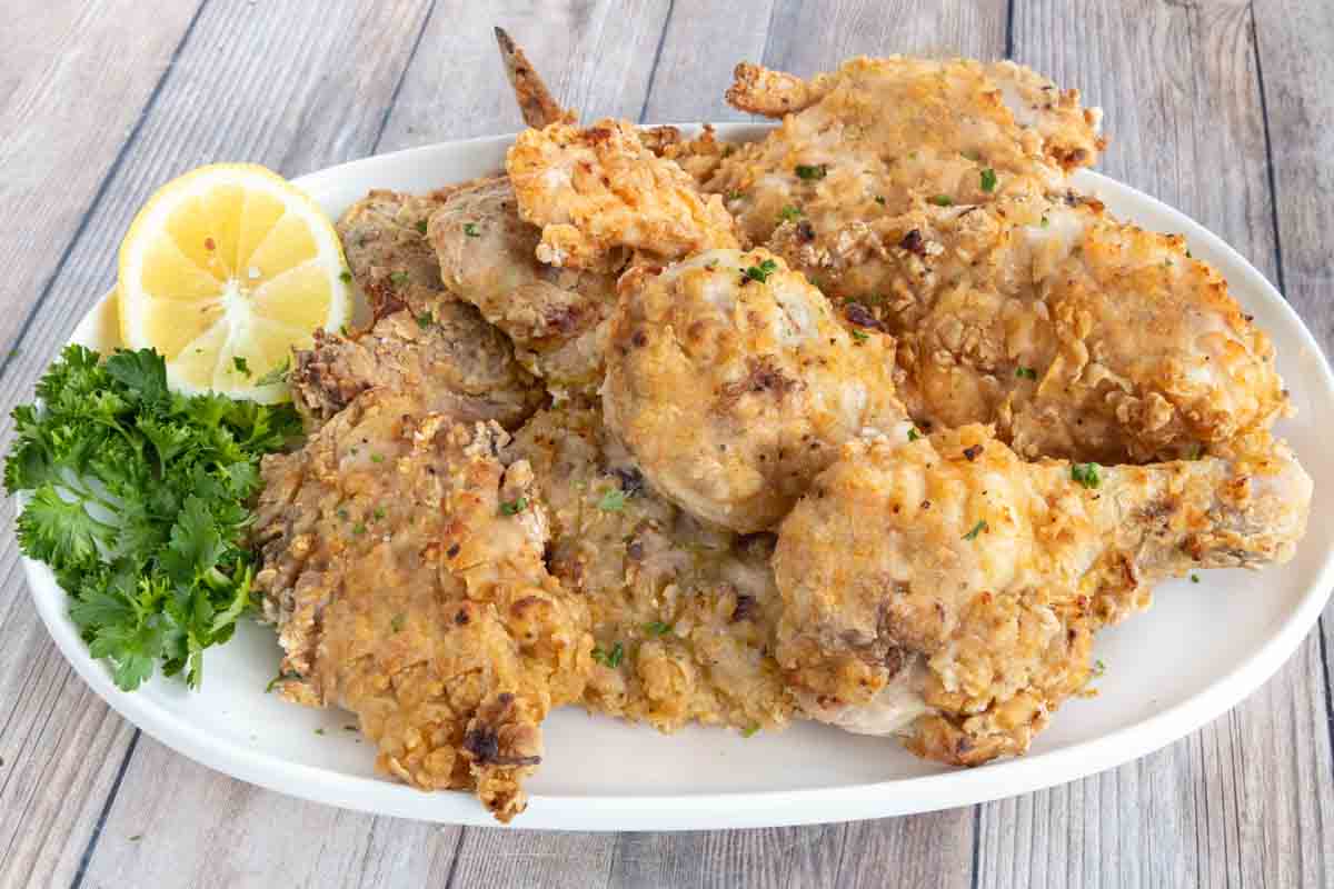 Oven fried chicken on a white platter with lemon and parsley.