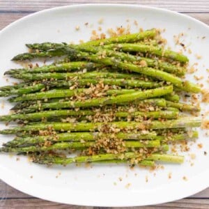 Roasted asparagus spears topped with pangrattato on a white platter.