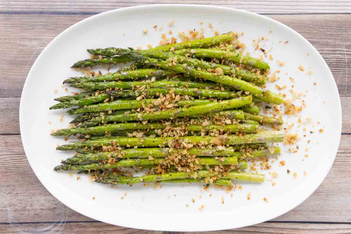 Roasted asparagus spears topped with pangrattato on a white platter.