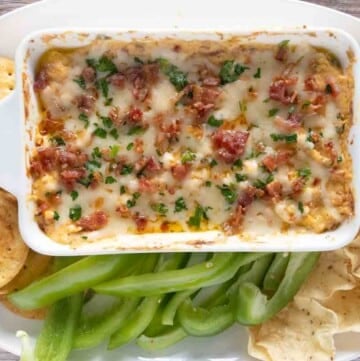 Baked crack dip in white casserole with crackers, tortilla chips and veggies.