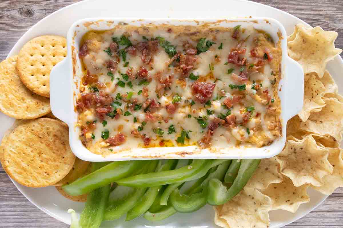 Baked crack dip in white casserole with crackers, tortilla chips and veggies.