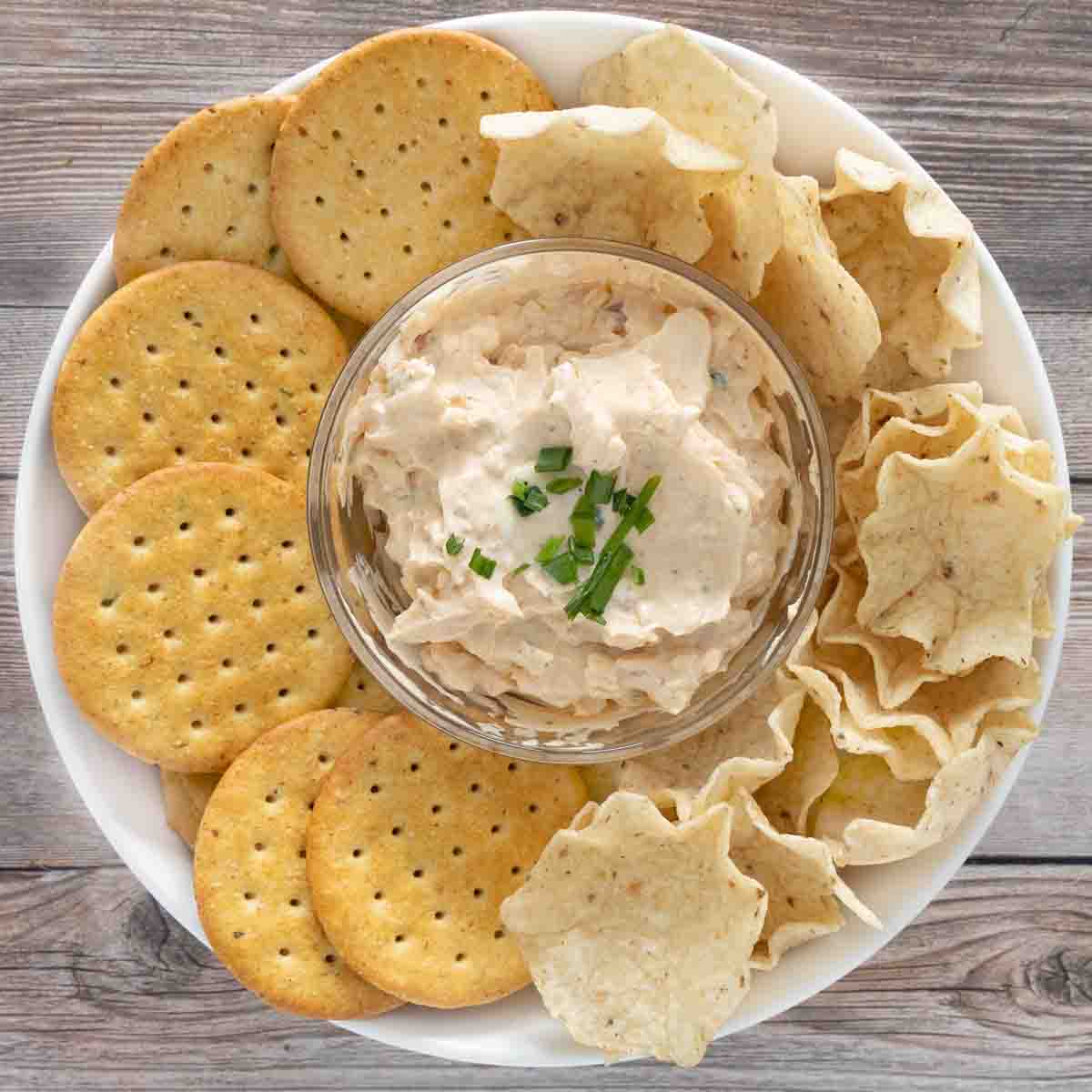 Cold crack dip in glass bowl with crackers and tortilla chips.