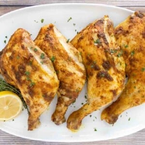 Four curry chicken quarters on a white platter with lemon.