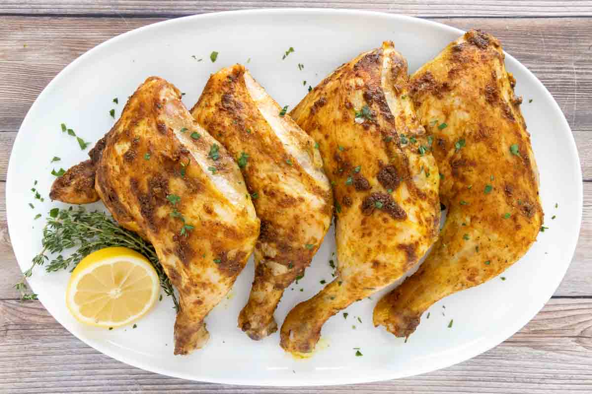Four curry chicken quarters on a white platter with lemon.