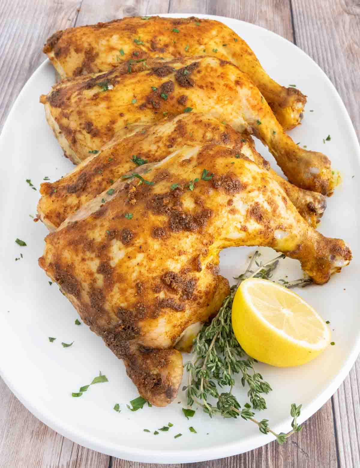 Four curry chicken quarters on a white platter with lemon.