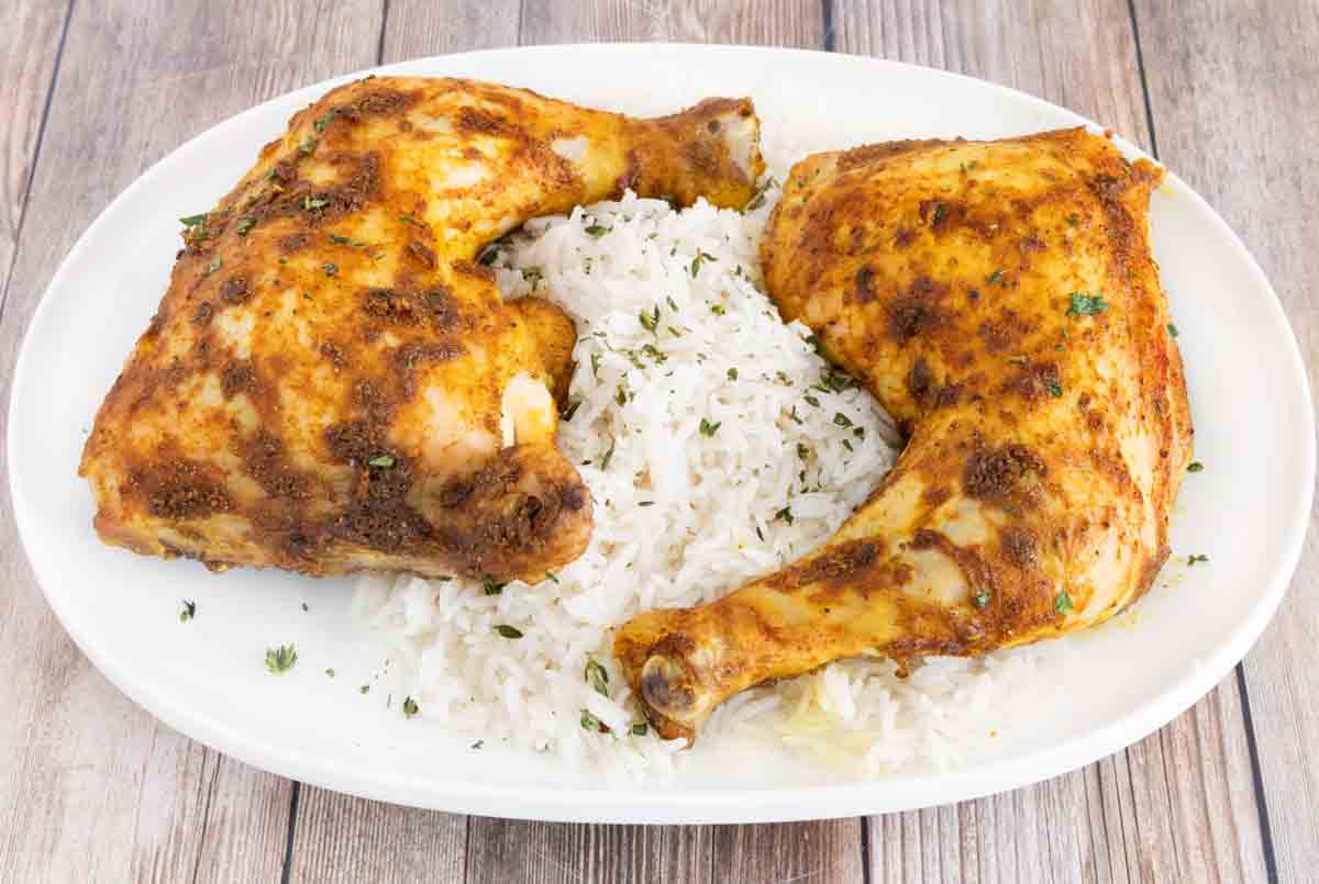 Two curry chicken quarters on a white platter with rice.