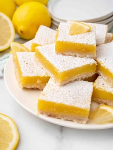 Lemon bars on a white platter with whole lemons in the background.