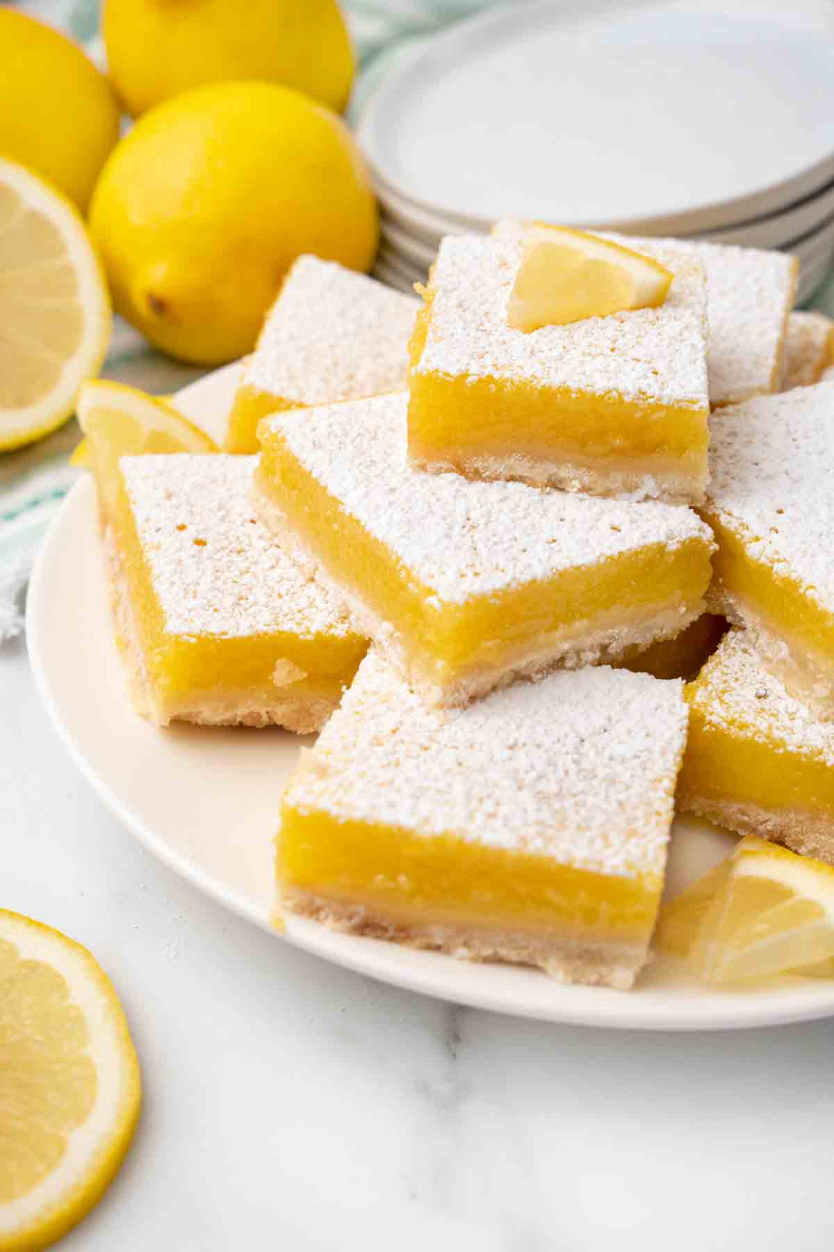 Lemon bars on a white platter with whole lemons in the background.