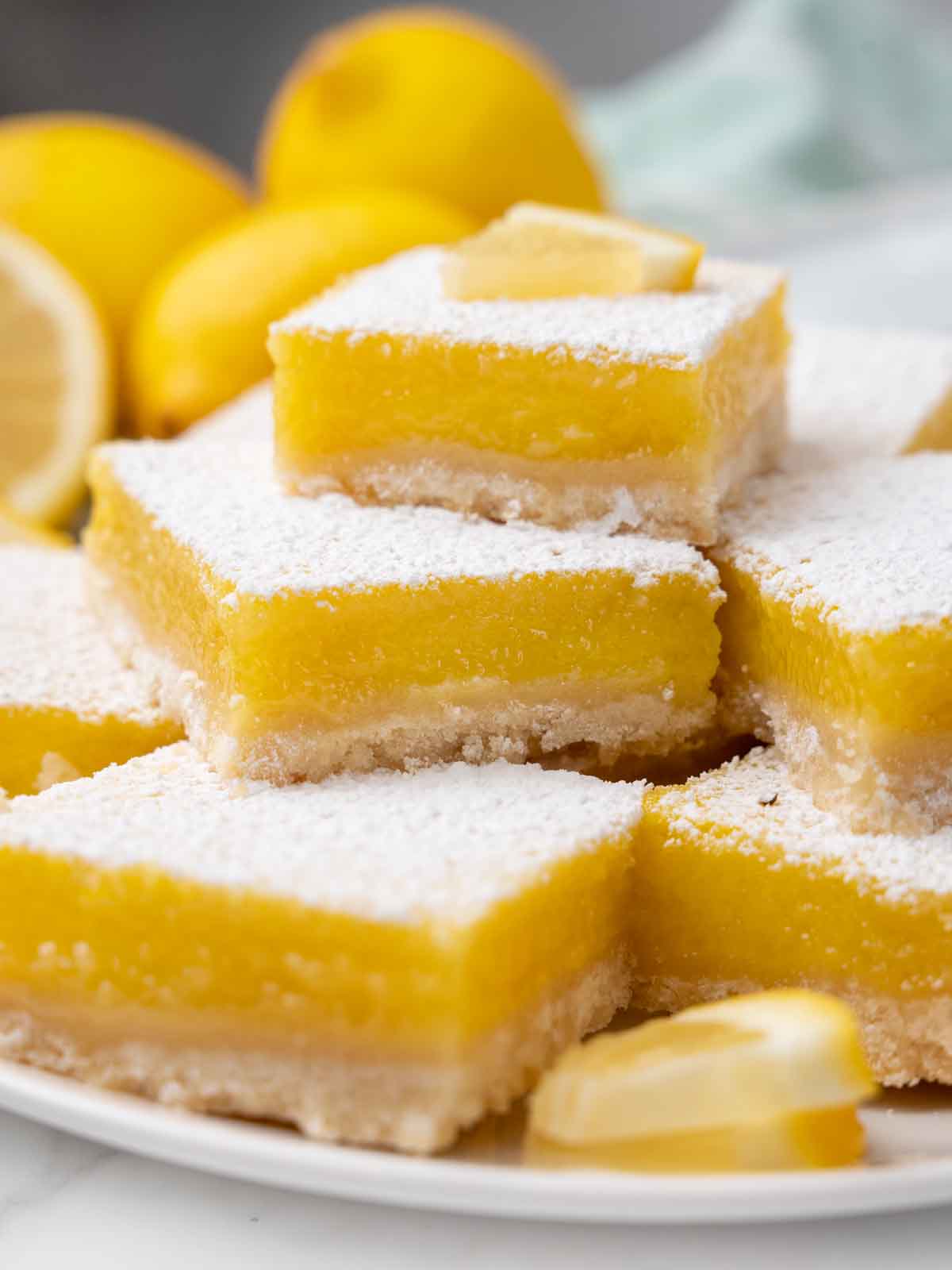Lemon bars on a white platter with whole lemons in the background.