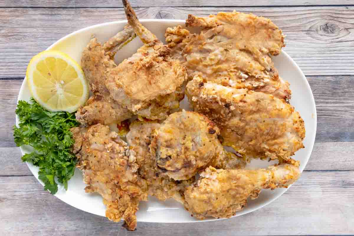 Oven fried chicken on a white platter with lemon and parsley.