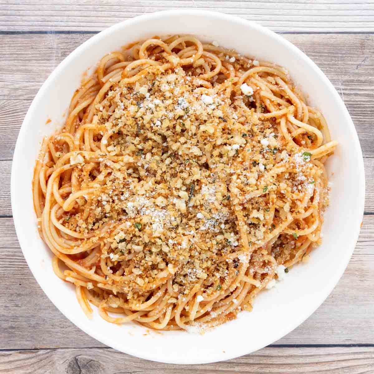 Spaghetti with red sauce topped with pangrattato and grated cheese in a white bowl.