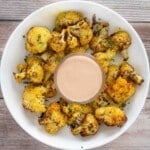 Oven roasted cauliflower with sriracha sauce in a white bowl.