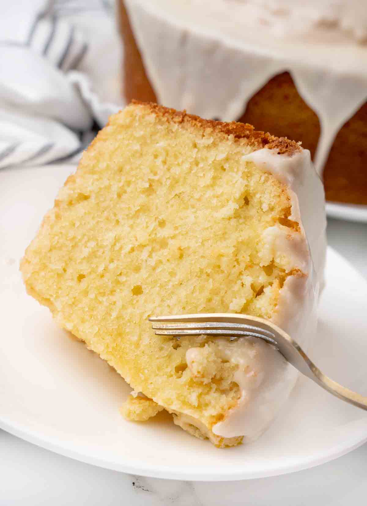 Slice of million dollar pound cake on a white plate with a fork in the cake.