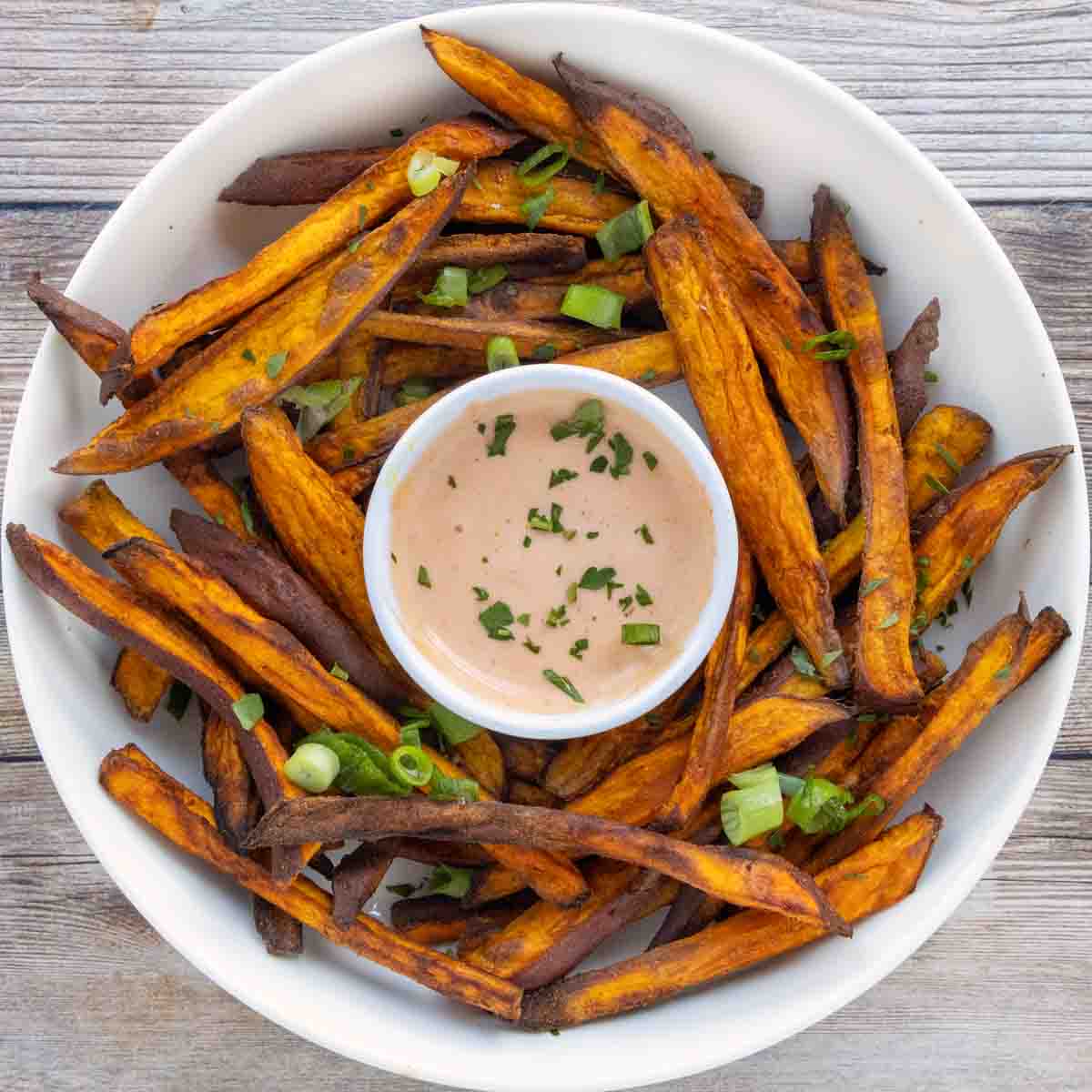 Air fryer sweet potato fries with sriracha mayo in a white bowl.