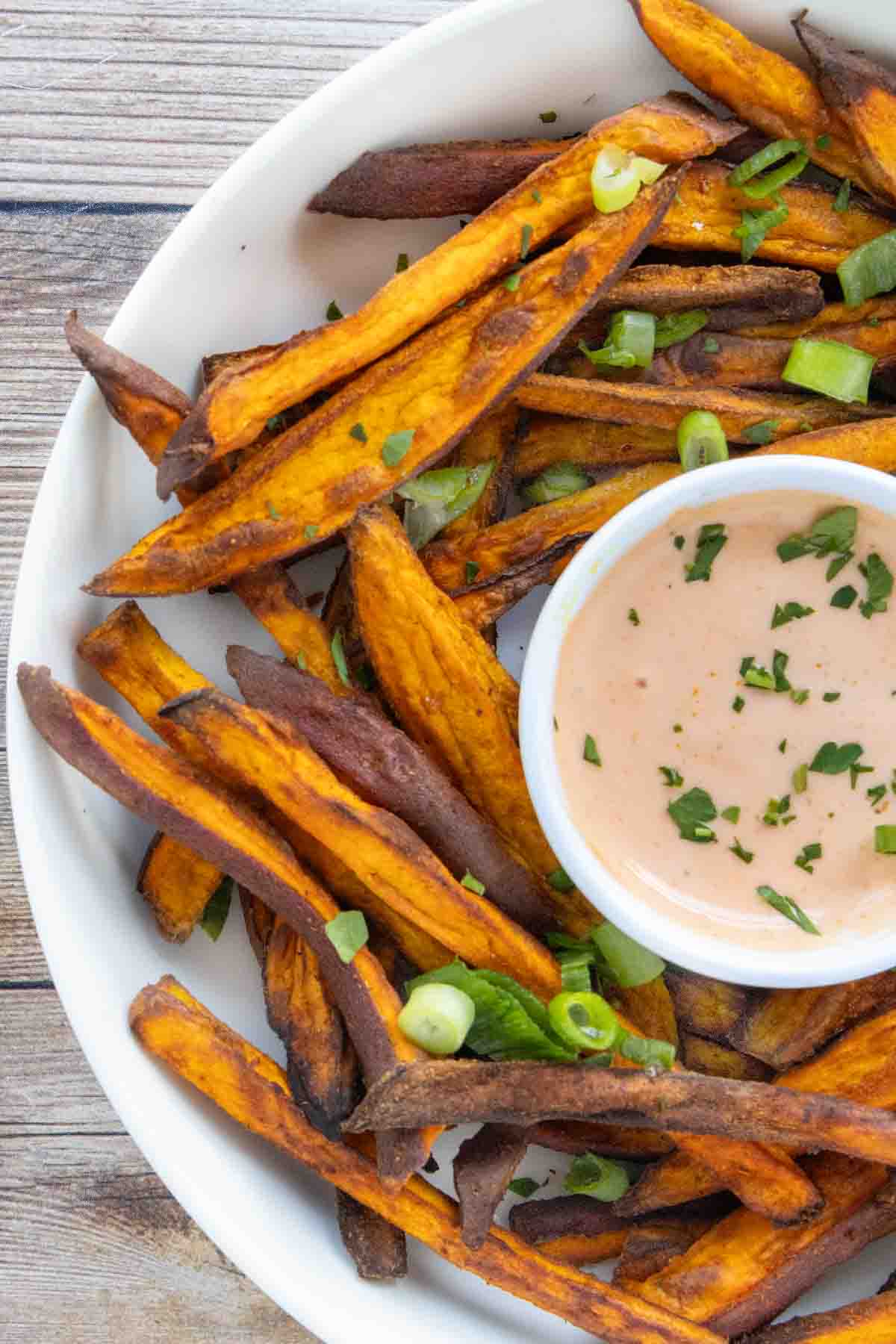 Air fryer sweet potato fries with sriracha mayo in a white bowl.