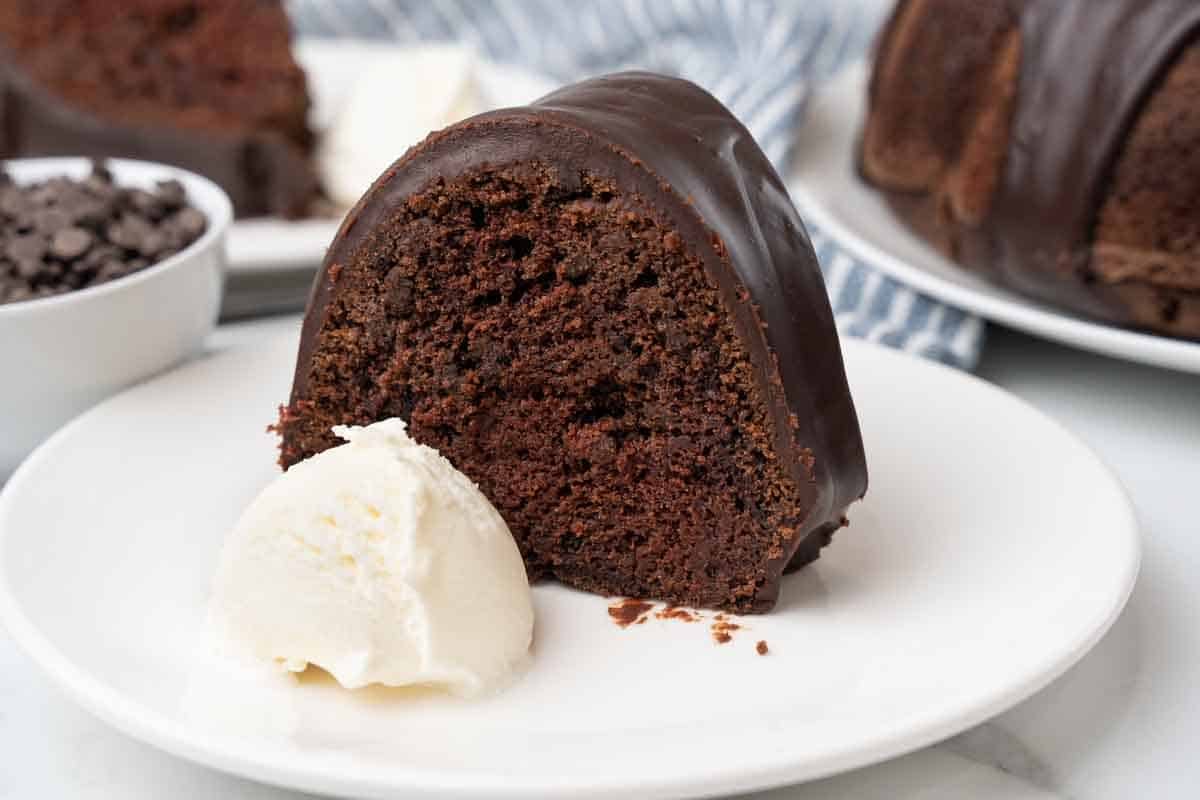 Slice of chocolate bundt cake with scoop of vanilla ice cream on a white plate.