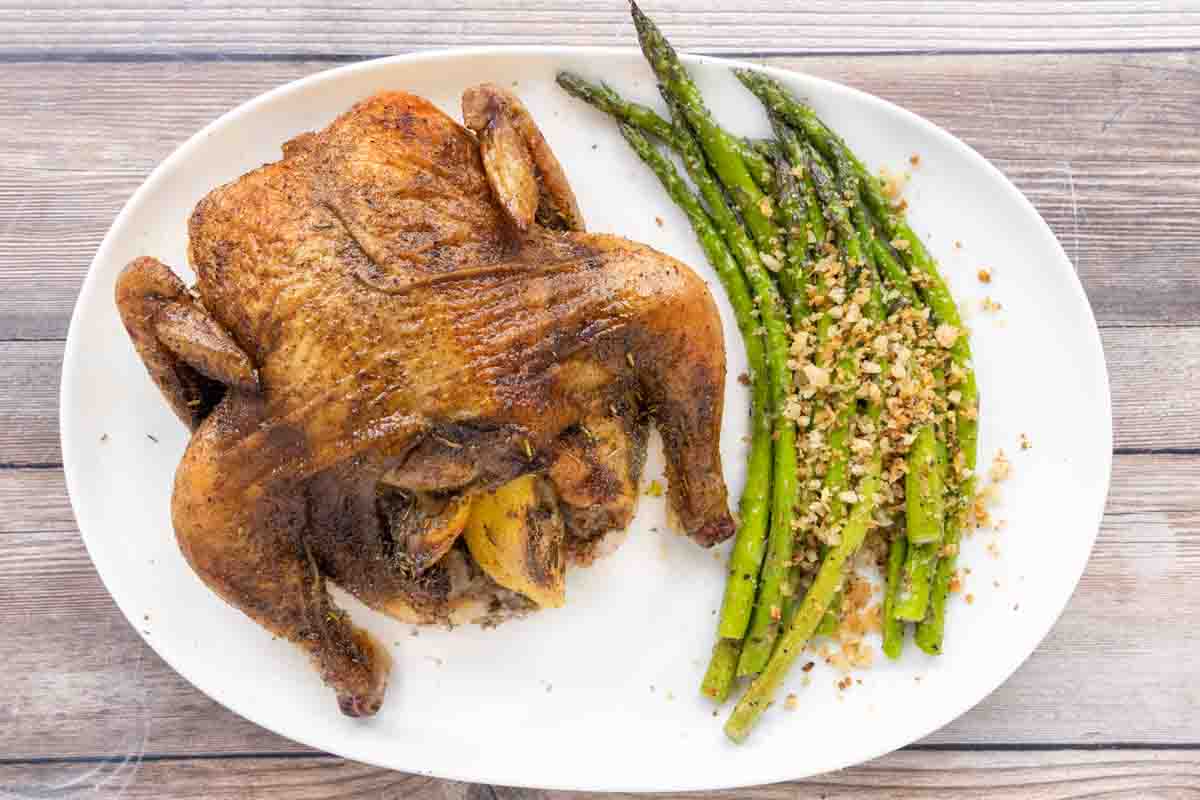 Roasted Cornish hen with asparagus on a white platter.