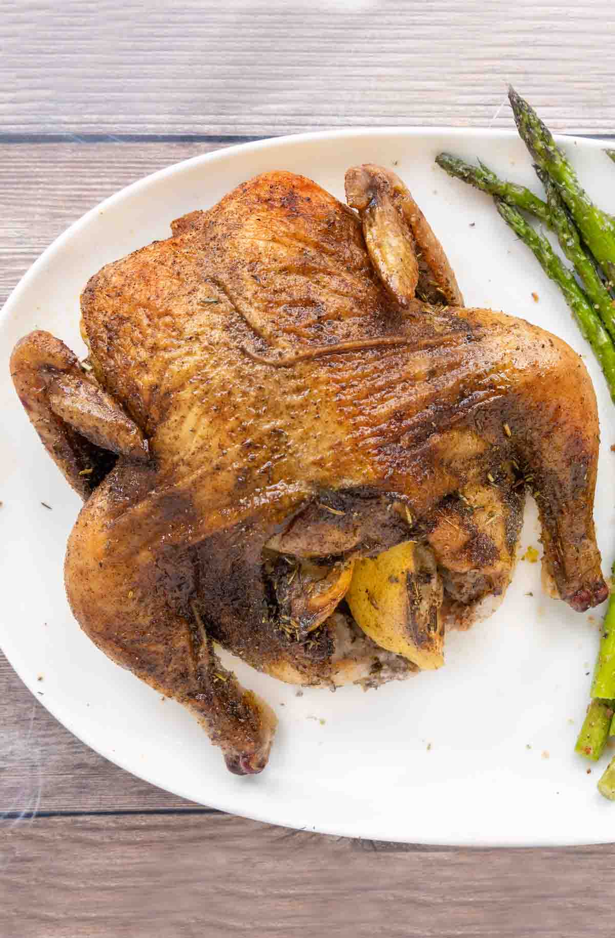 Roasted Cornish hen with asparagus on a white platter.